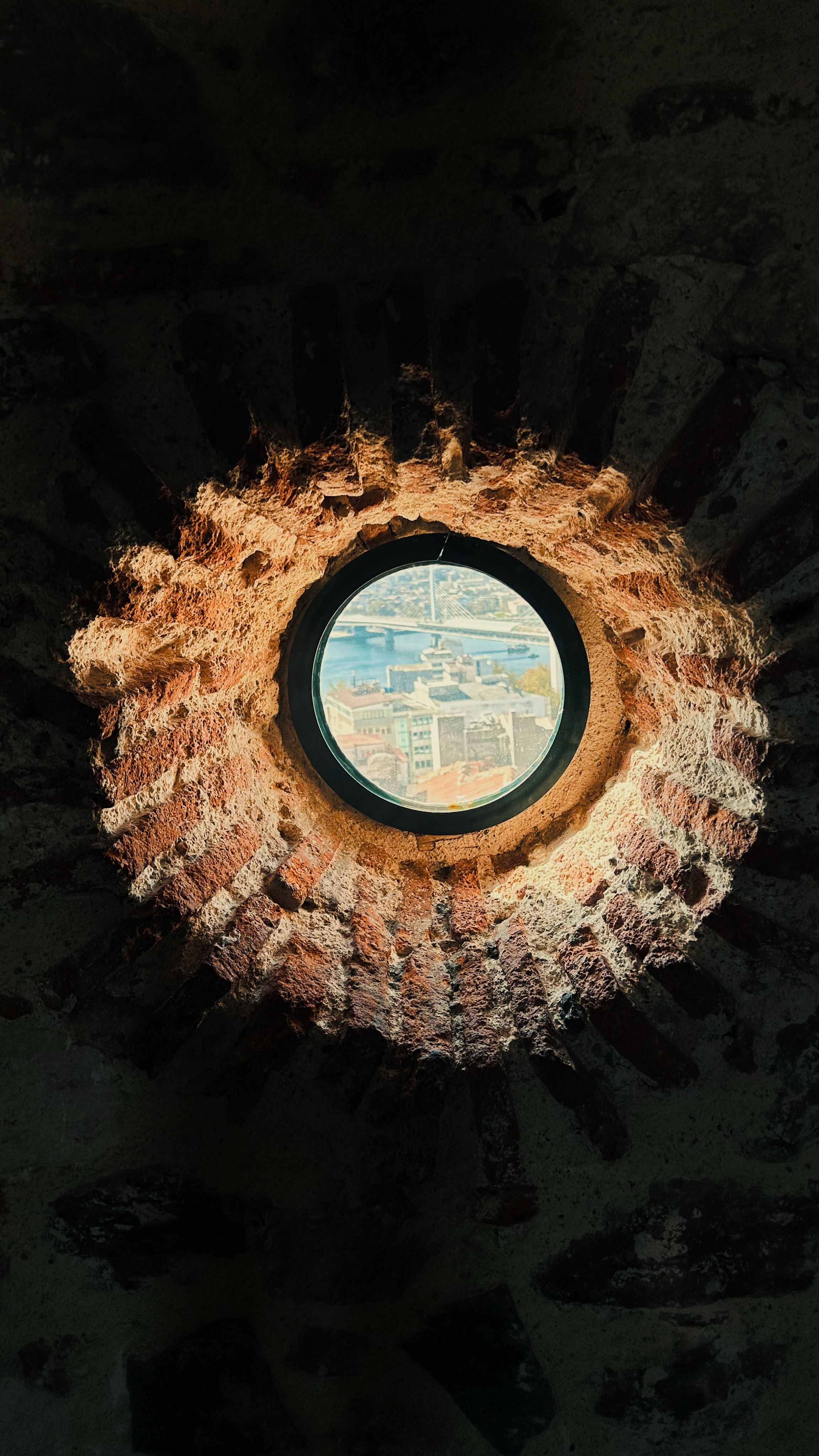 Round brick window offering a unique view of the cityscape under sunlight.