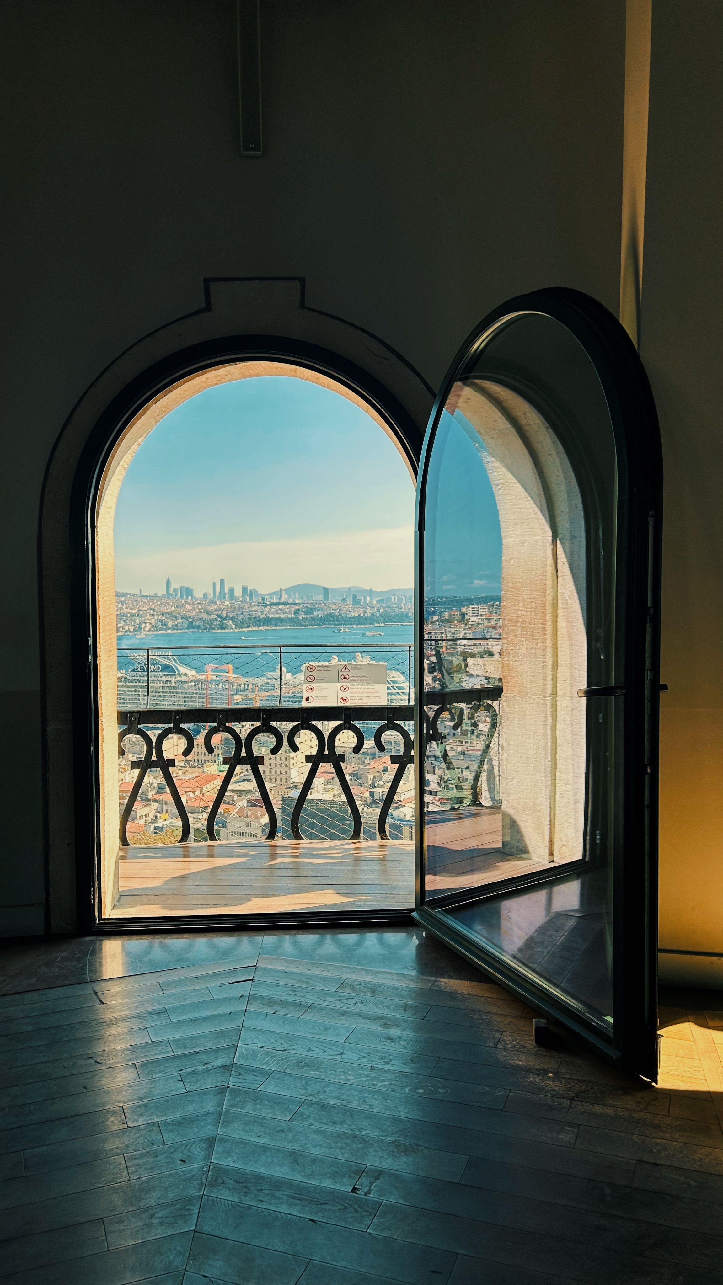 A breathtaking view of a city skyline and sea through an arched window, featuring intricate ironwork.