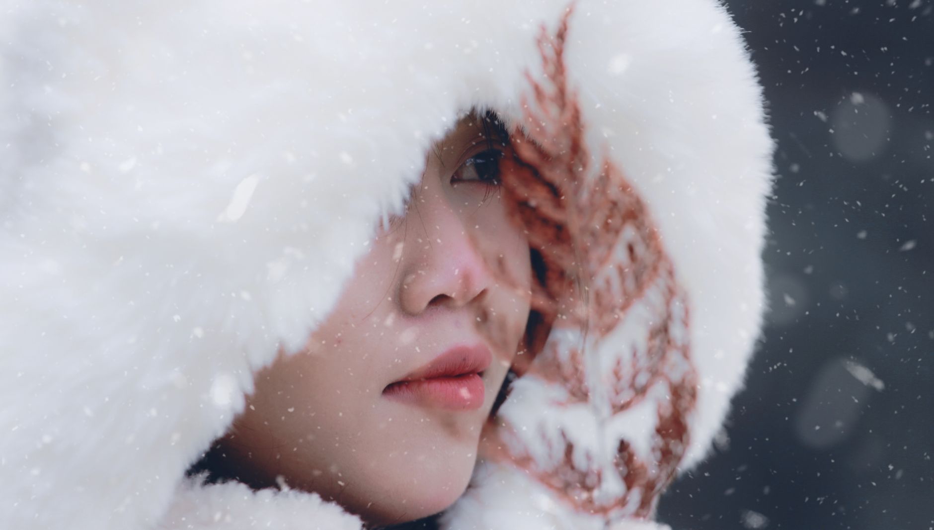 Close-up portrait of a woman in a fur hood during snowfall.