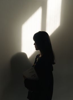 A moody silhouette of a woman standing against a wall with dramatic lighting and shadows.