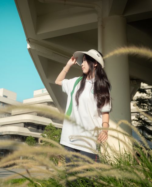 Free Young woman wearing hat, standing outdoors by unique architecture, bathed in sunlight. Stock Photo