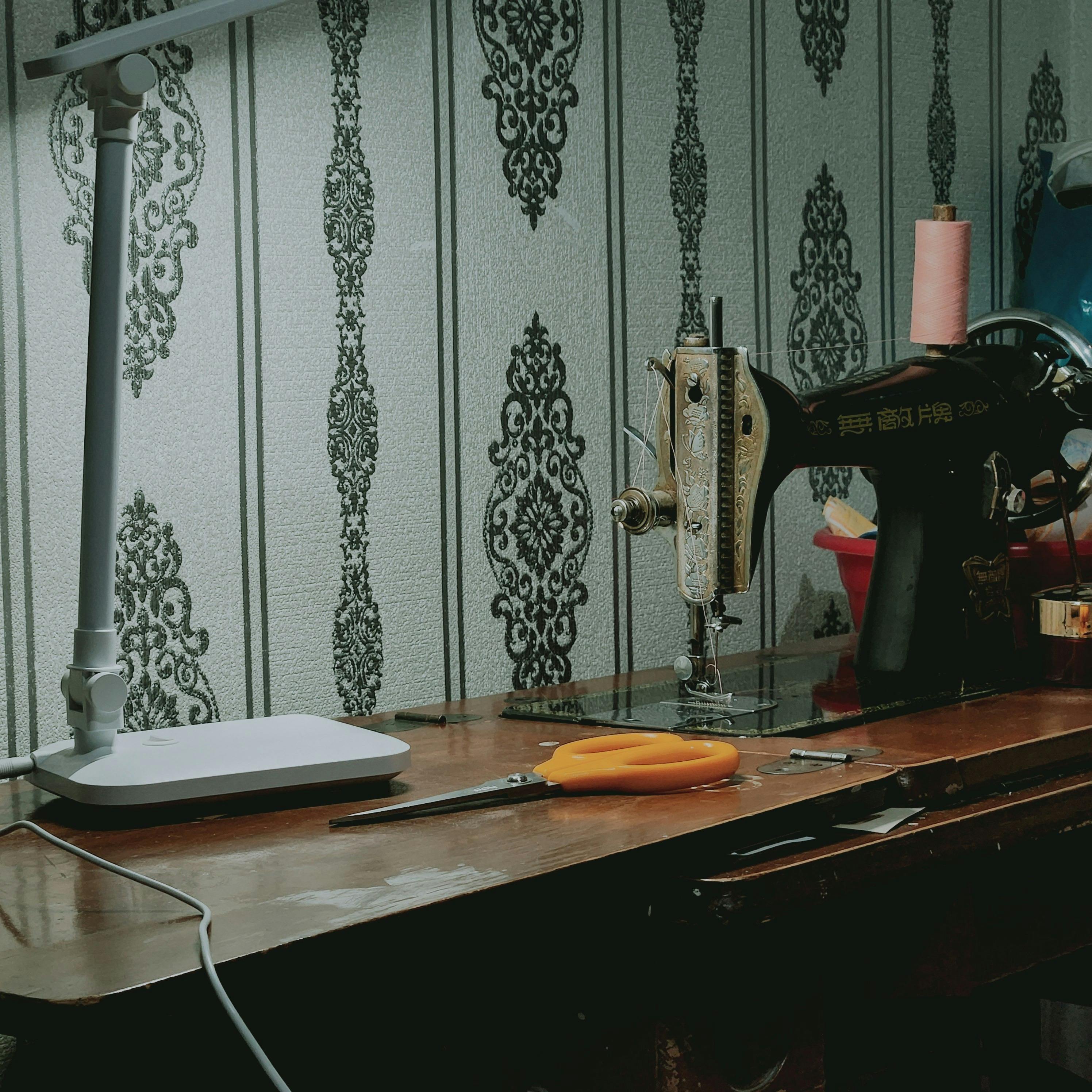 A classic sewing machine on a wooden desk with sewing tools, set in a cozy, vintage-style home studio.
