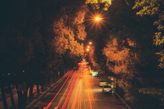 Long exposure of a night street scene in Kermanshah, Iran, featuring car light trails under streetlights.