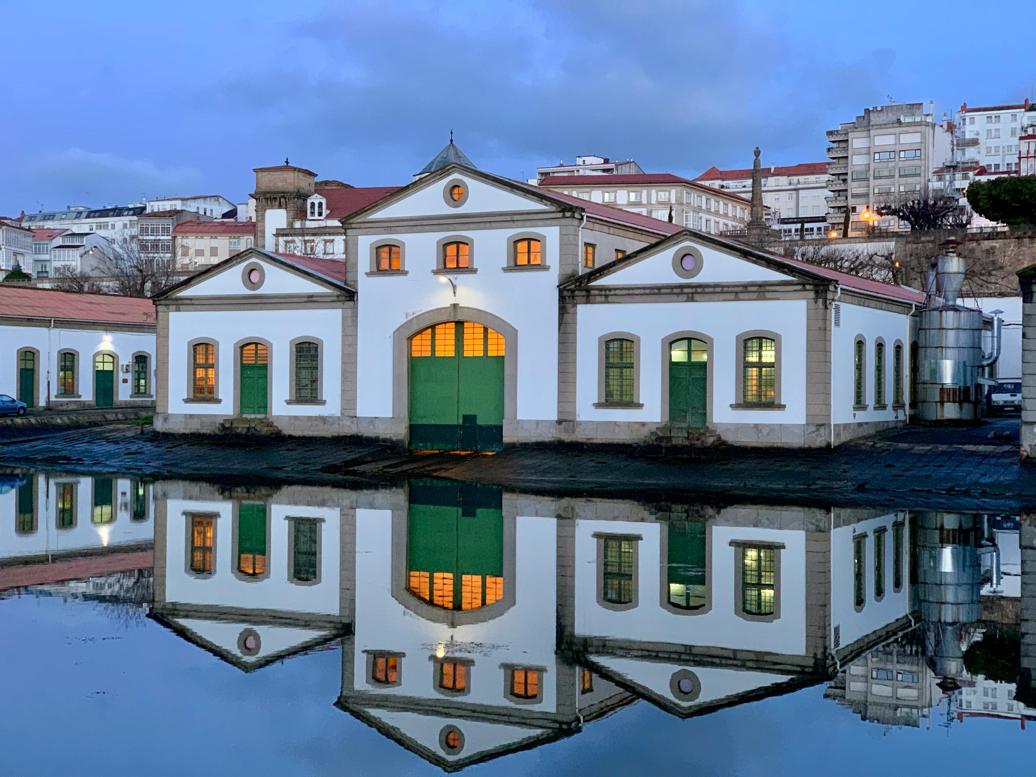 Historic industrial building with symmetrical reflection on calm water at twilight, creating a serene ambiance.