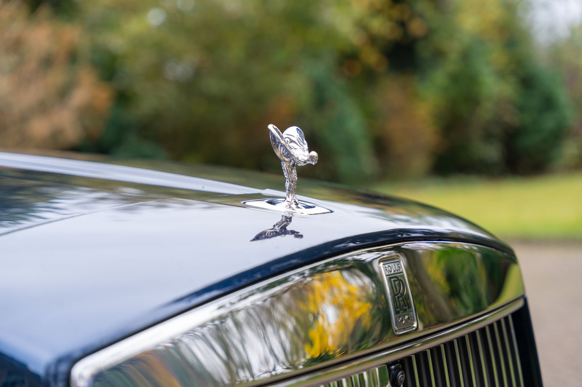 Close-up of a Rolls Royce hood ornament reflecting elegance and luxury in a natural outdoor setting.