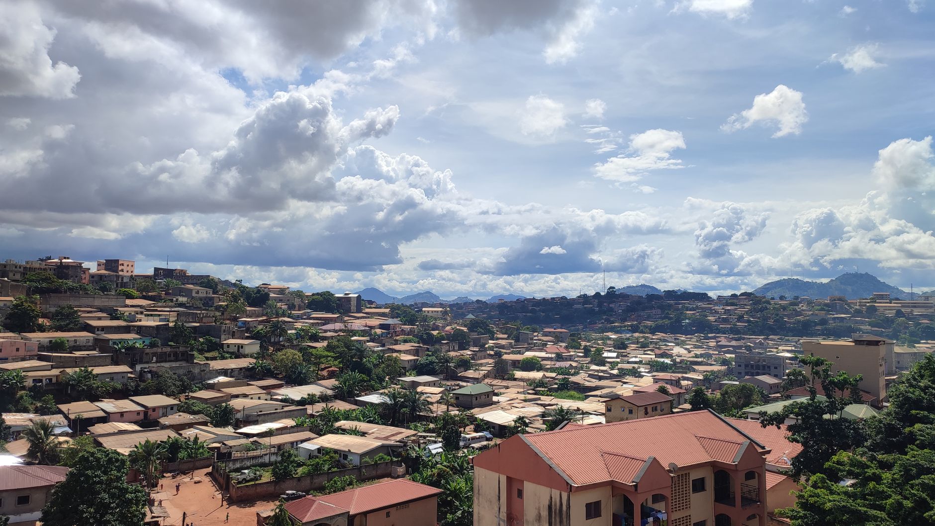 Aerial view of Yaoundé, Cameroon showcasing rooftops and lush greenery under a cloudy sky.