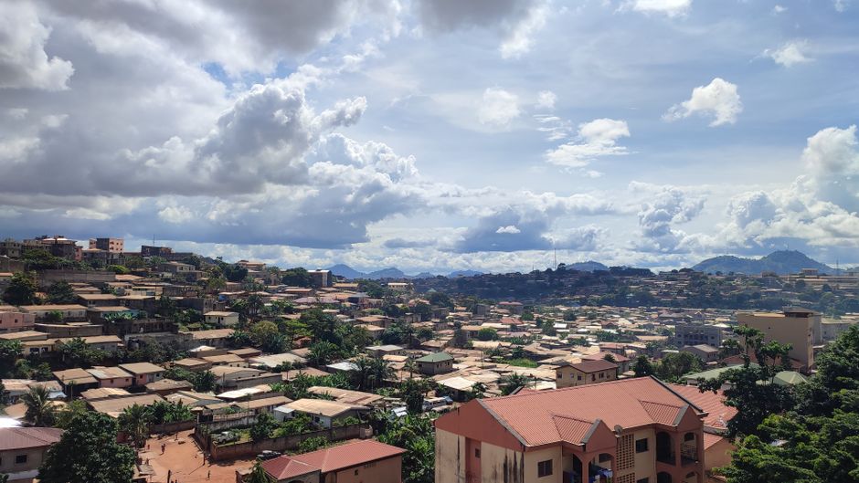 Aerial view of Yaoundé, Cameroon showcasing rooftops and lush greenery under a cloudy sky.