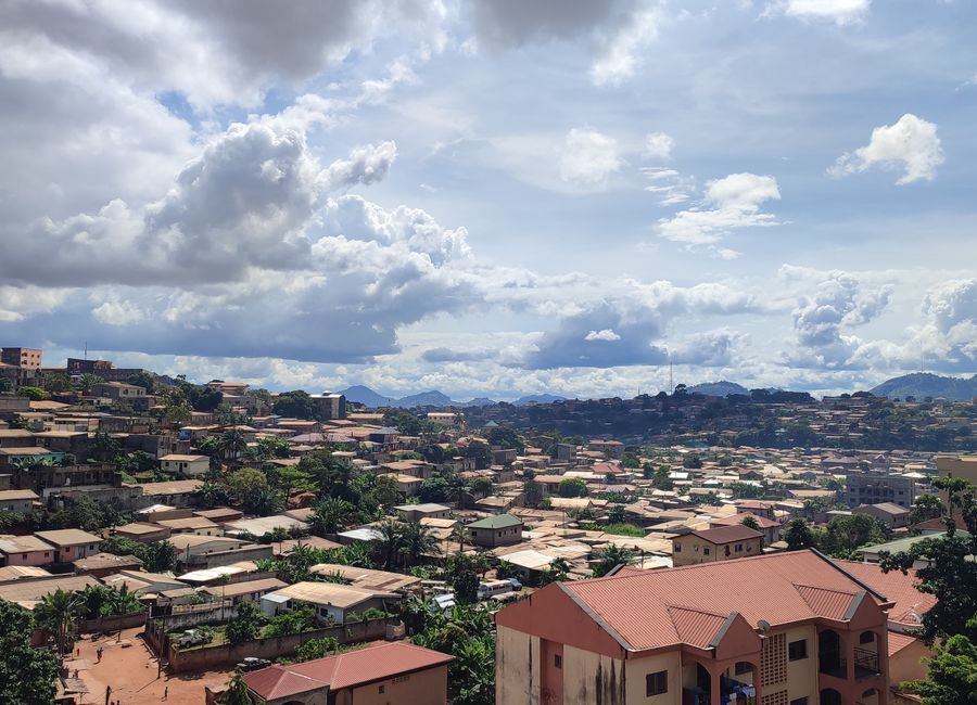 Aerial view of Yaoundé, Cameroon showcasing rooftops and lush greenery under a cloudy sky.