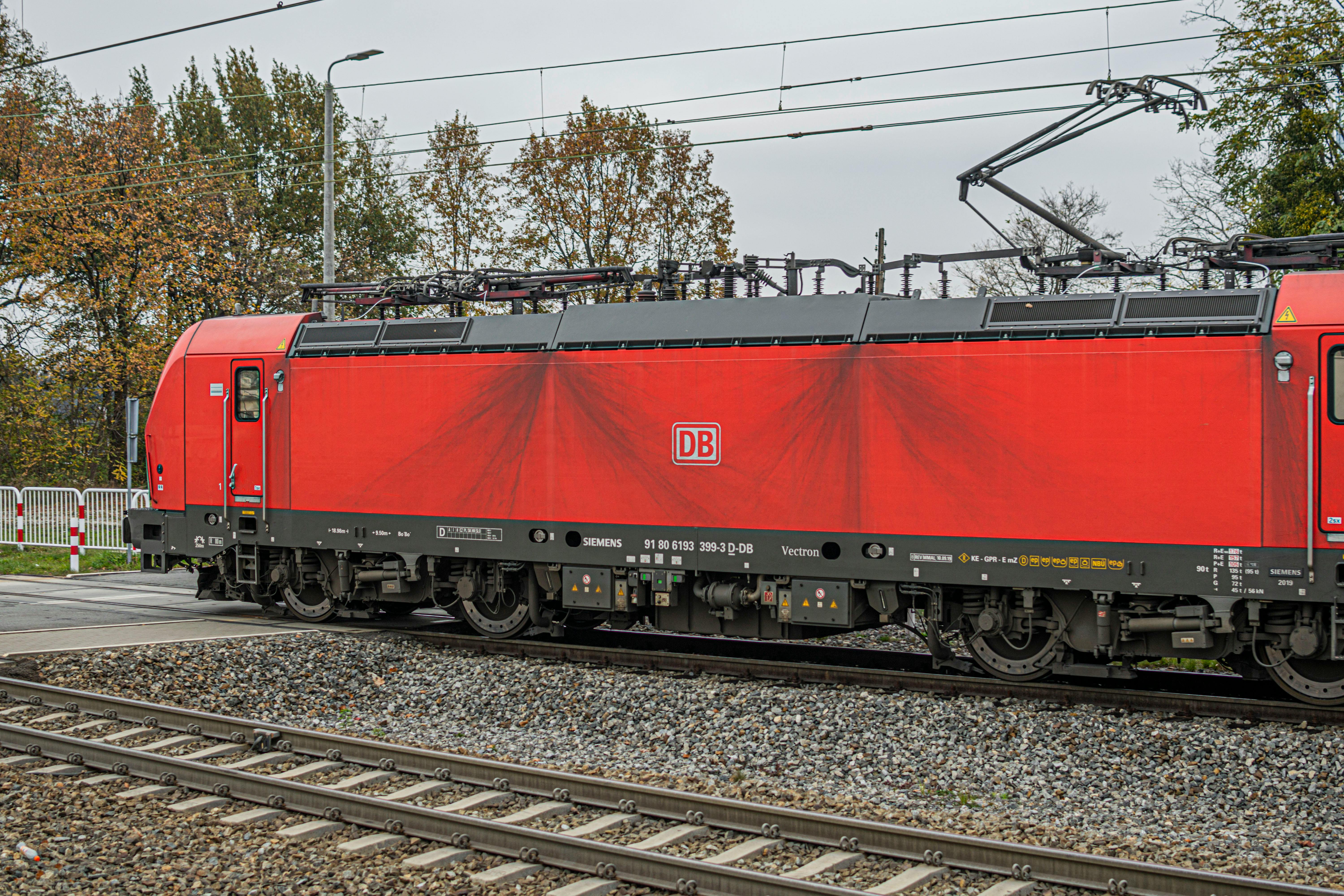 A bright red DB train locomotive at a railroad crossing on an overcast day.