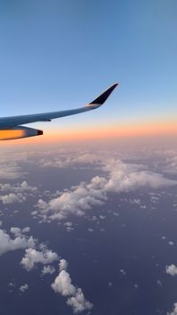 View from an airplane window of a wing above clouds during a serene sunset.