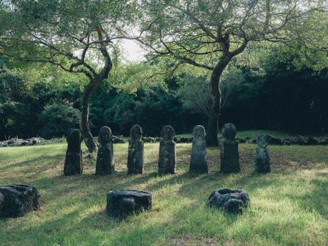 Row of Jangseung stone statues under trees in Seoul park setting.