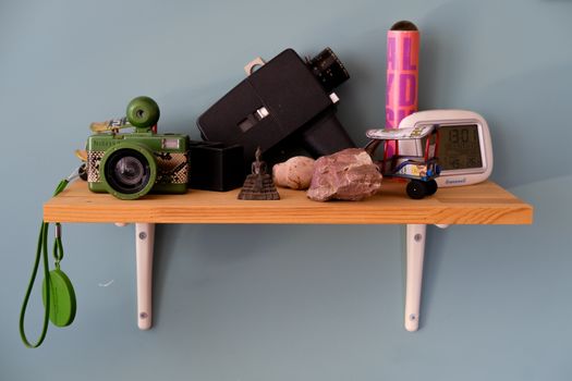A wooden shelf displaying a camera, stones, a figurine, and a model truck against a teal wall.