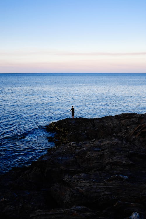 Person Standing on Rock Beside Body of Water