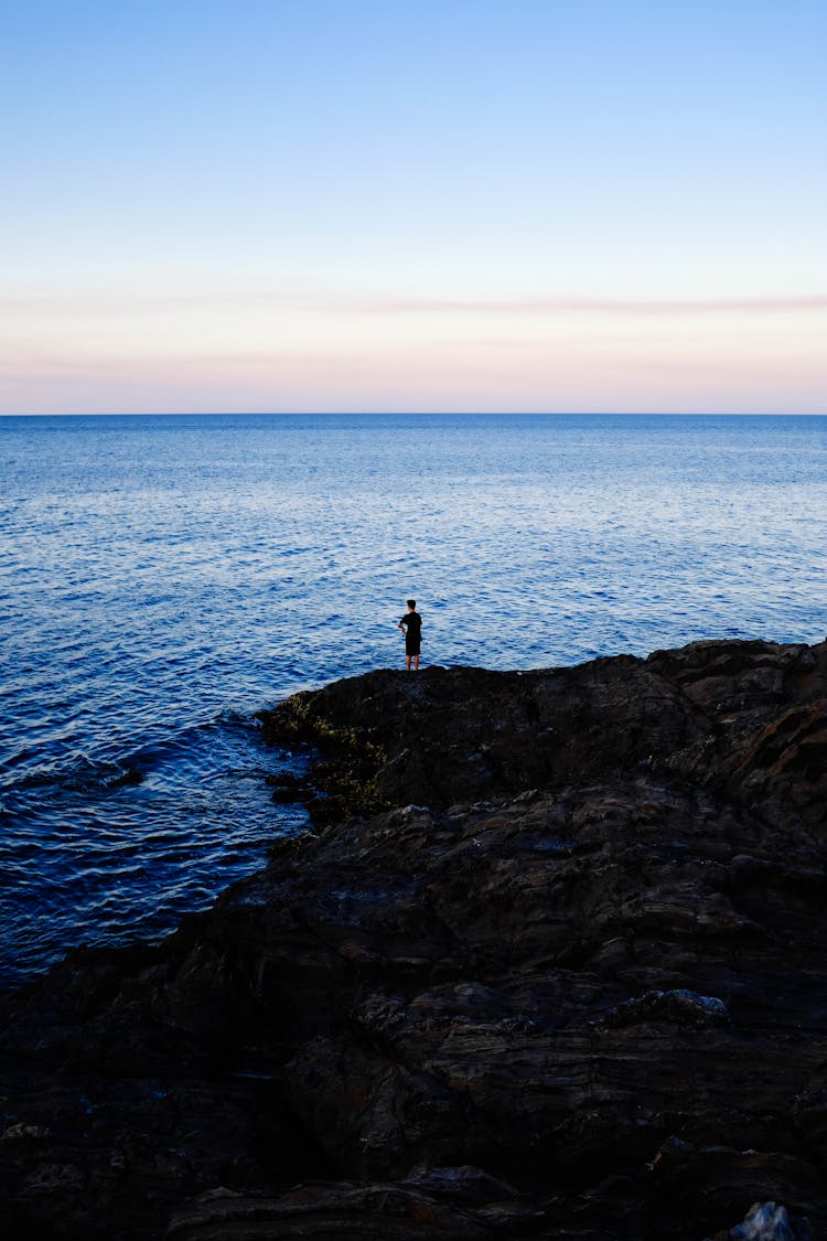 Person Standing On Rock Beside Body Of Water