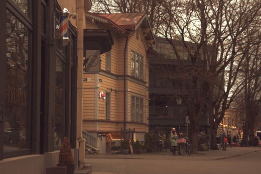 Street scene in Tallinn, Estonia with wooden houses, a barber pole, and people walking on an autumn day.