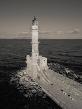 A stunning aerial shot of a classic stone lighthouse on a rocky pier against a serene sea backdrop.