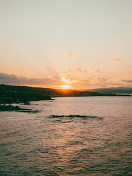 A breathtaking aerial view of a serene coastal sunset over the ocean, capturing golden hues and tranquil waters.
