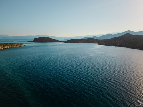 Free A serene aerial view of a beautiful coastal landscape with clear blue waters and distant mountains under a sunny sky. Stock Photo