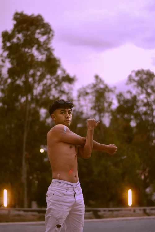 Free A young man stretches outdoors during twilight, surrounded by trees, creating a calm atmosphere. Stock Photo