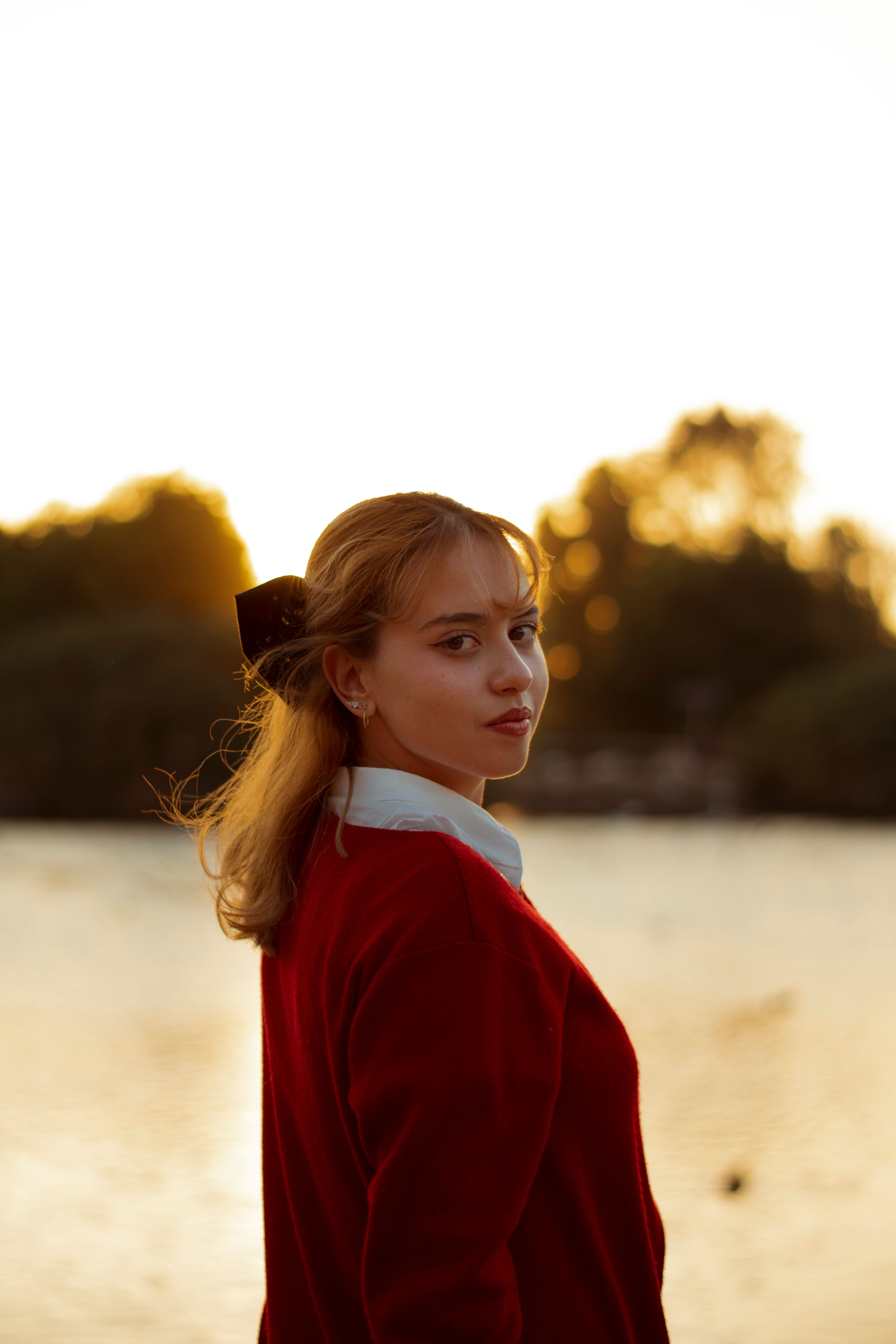 Portrait of a young woman in a red sweater by the lake at sunset.