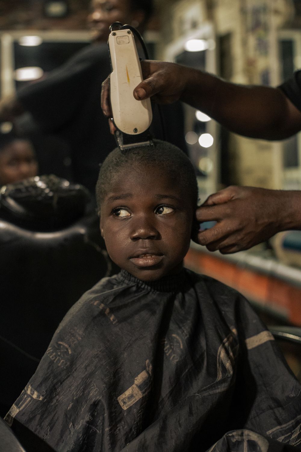 Barber running clippers over a young boy's hair while he sits in the chair