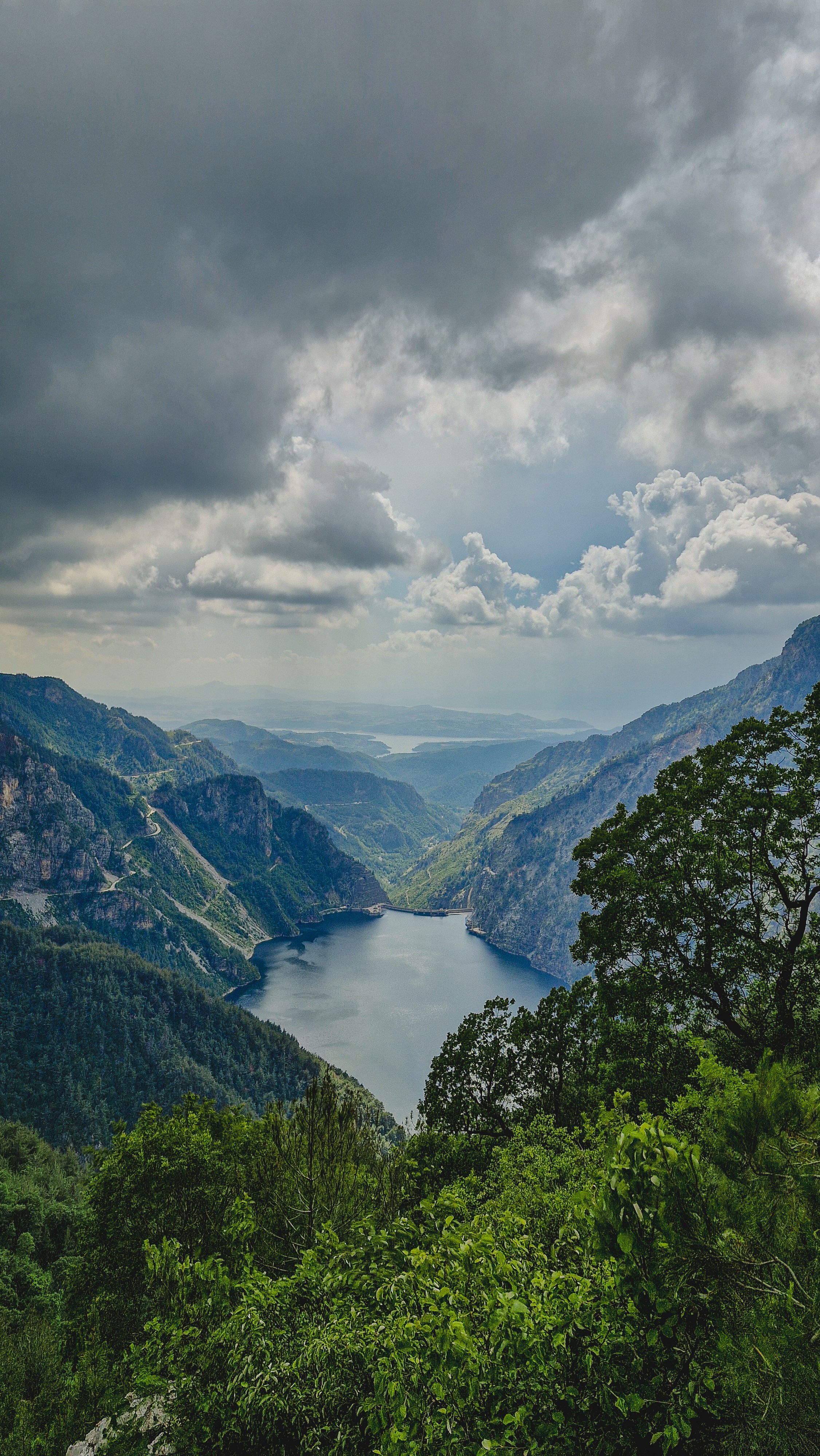 Breathtaking aerial view of a mountain lake surrounded by lush greenery and dramatic cloud formations.