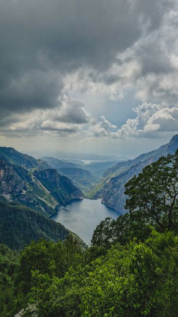 Breathtaking aerial view of a mountain lake surrounded by lush greenery and dramatic cloud formations.