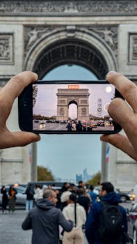 Tourists capture Paris's iconic Arc de Triomphe on a busy autumn day.