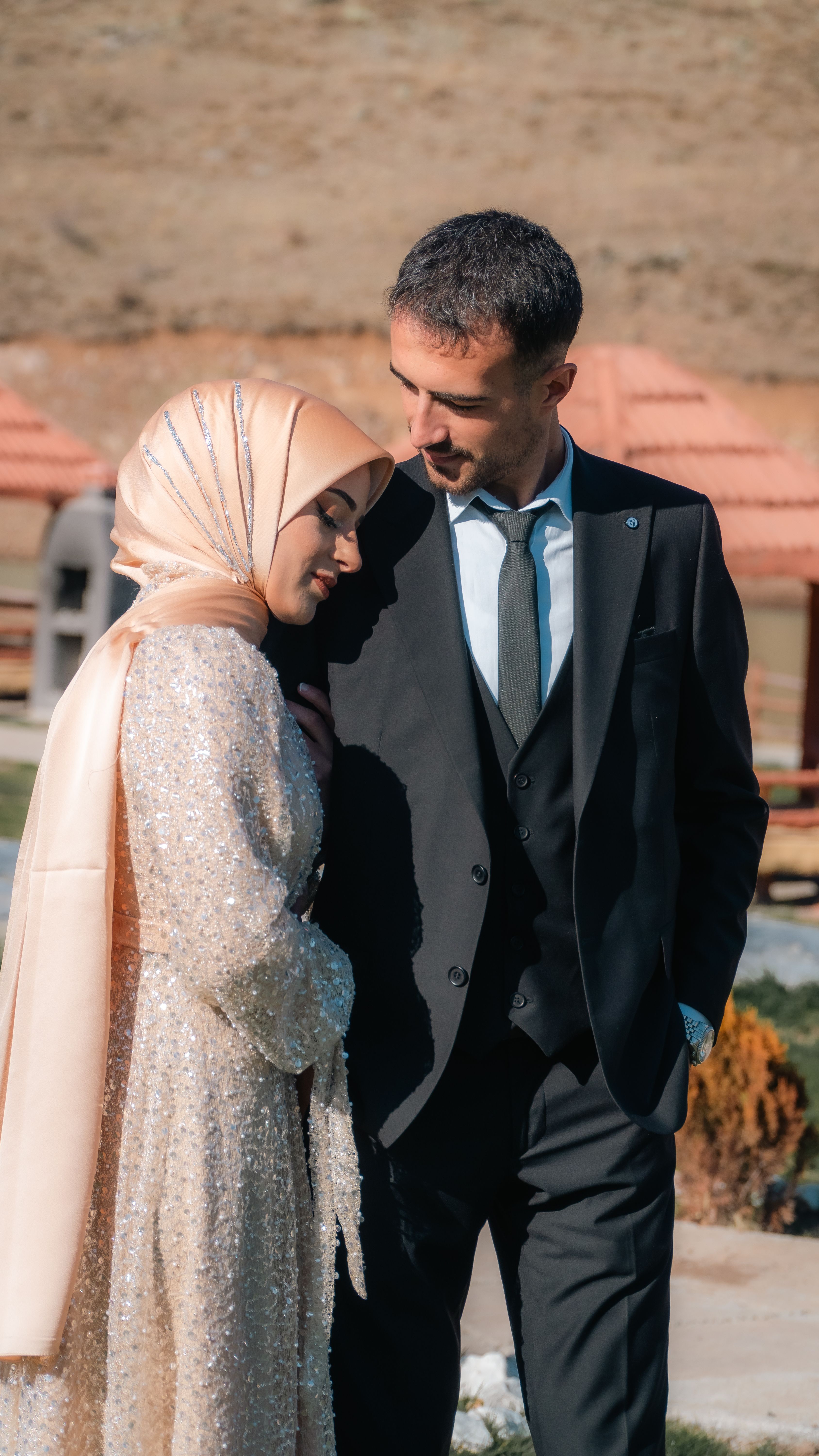 A charming outdoor photo of a bride in hijab and groom smiling tenderly at each other.