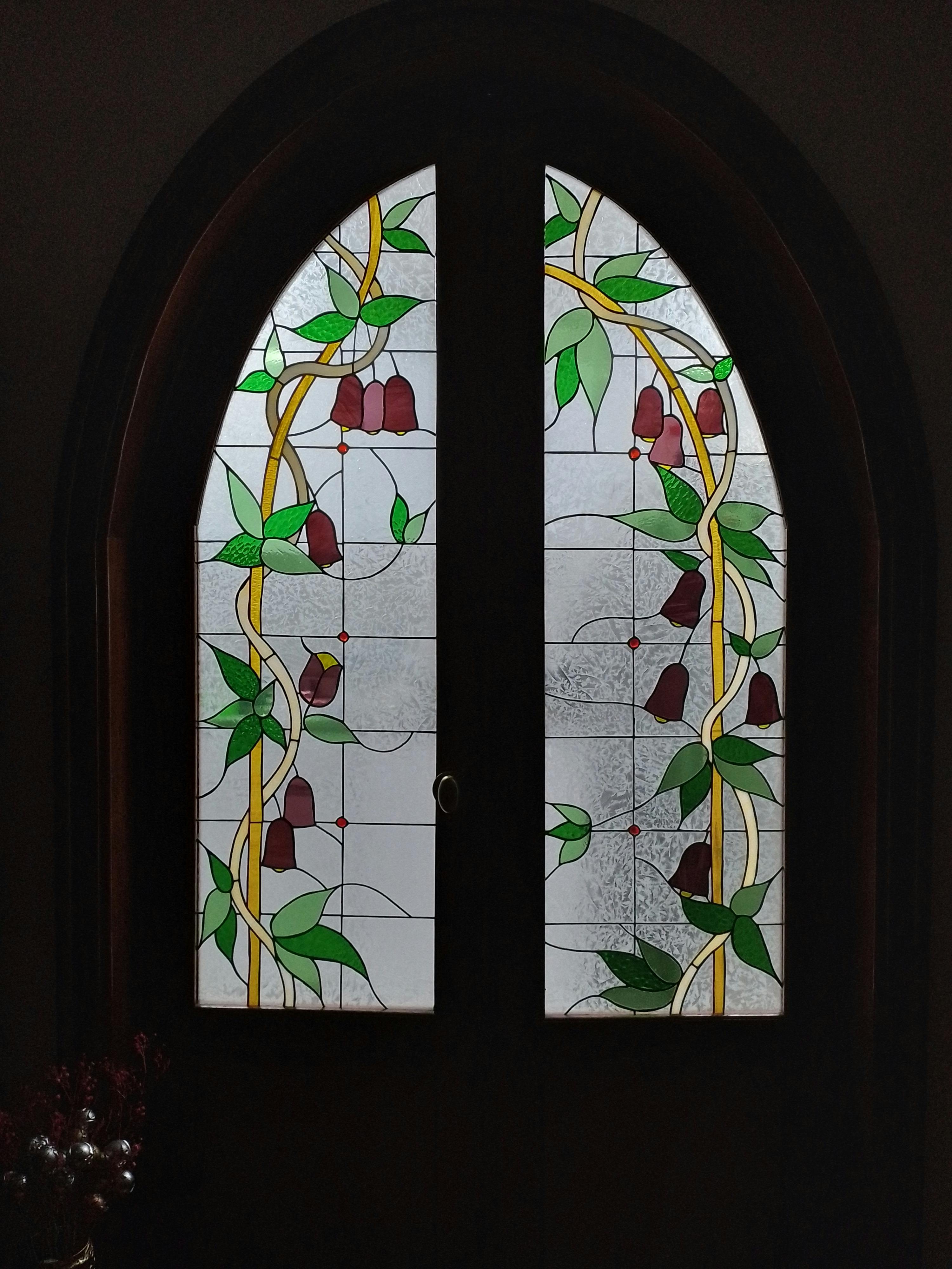 Artistic stained glass door featuring floral patterns and leaves in a dark setting.