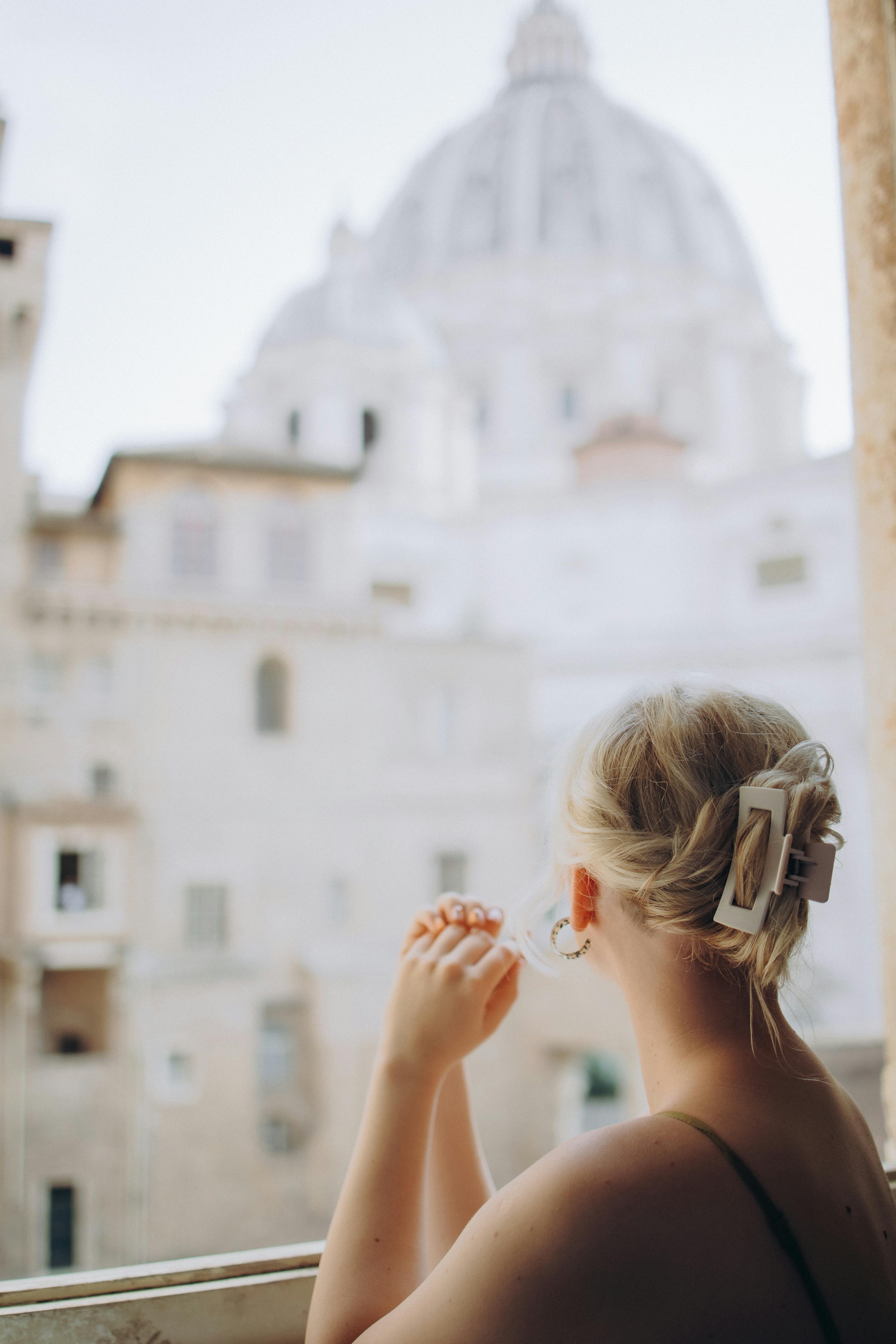 A contemplative scene of a woman looking out over Vatican City towards St. Peter's Basilica.