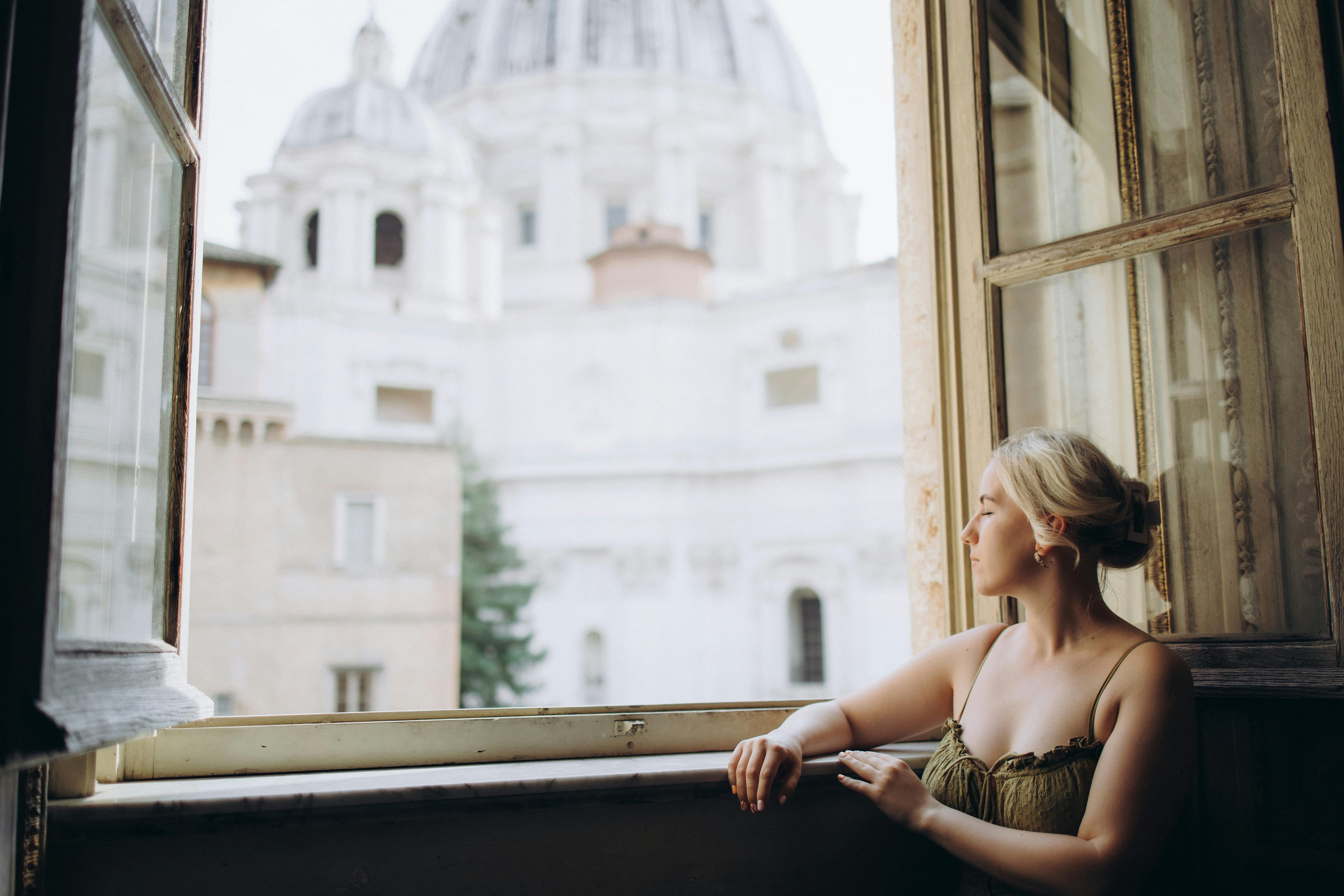 Young woman gazing out from a window with a view of St. Peter's Basilica in Vatican City.