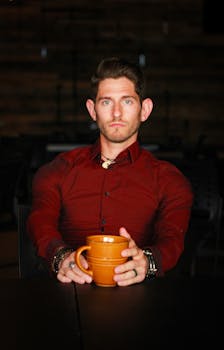 一位时尚男子穿着红色衬衫，在室内拿着咖啡杯，流露出自信