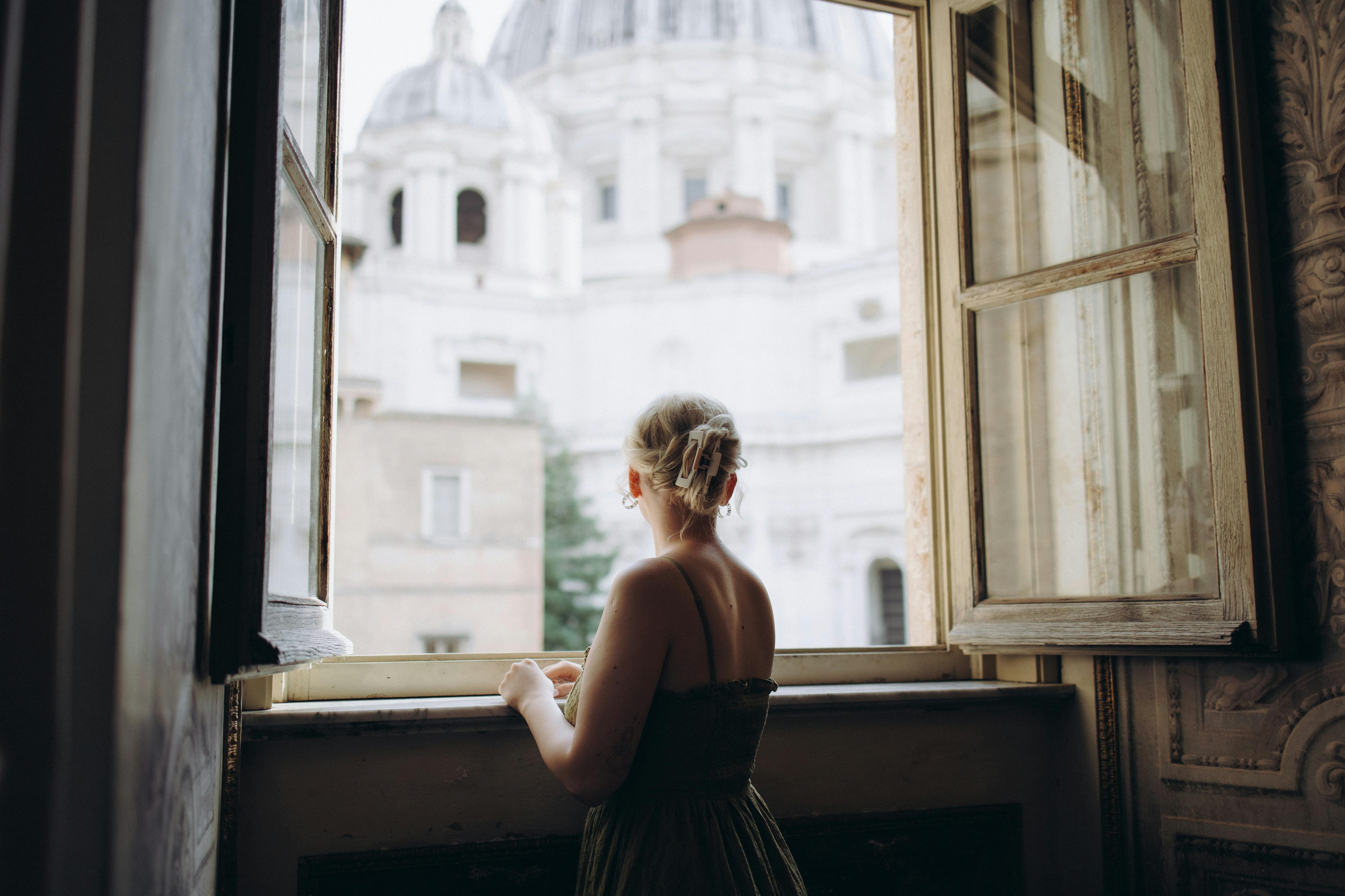 A woman looks out a window at St. Peter's Basilica in Vatican City, capturing a serene moment.