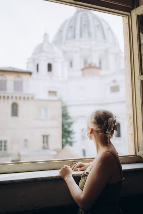 Free A woman gazes thoughtfully out a window with St. Peter's Basilica in the background. Stock Photo