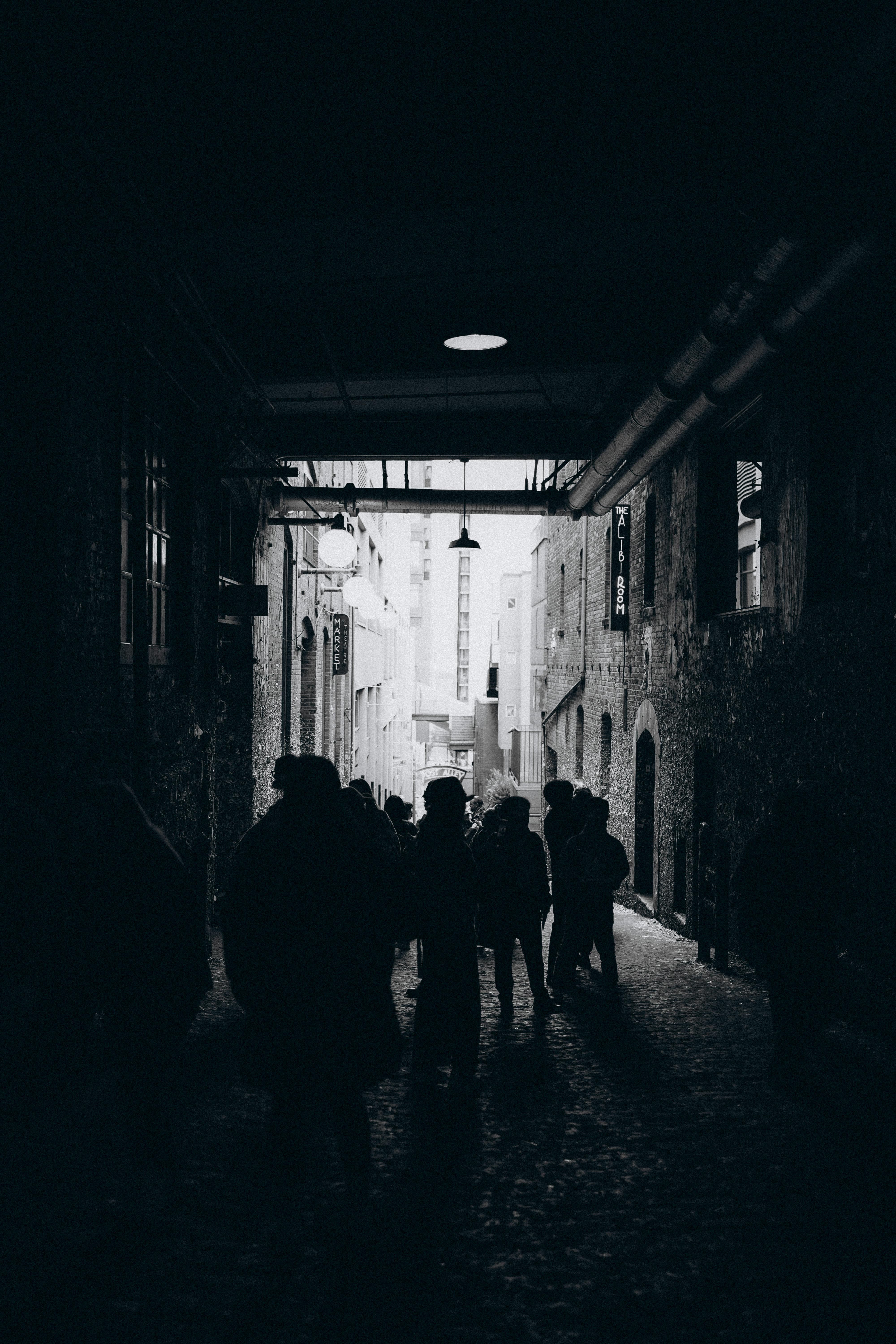 Silhouetted pedestrians in dark alleyway creating a moody urban atmosphere.