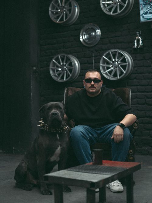 Free Man seated with strong dog in industrial room with wheel decor. Stock Photo