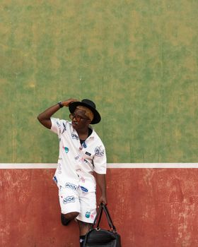 Stylish person posing casually with bag against colorful urban wall.