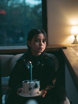 A young girl with a birthday cake and candle in a cozy indoor setting.