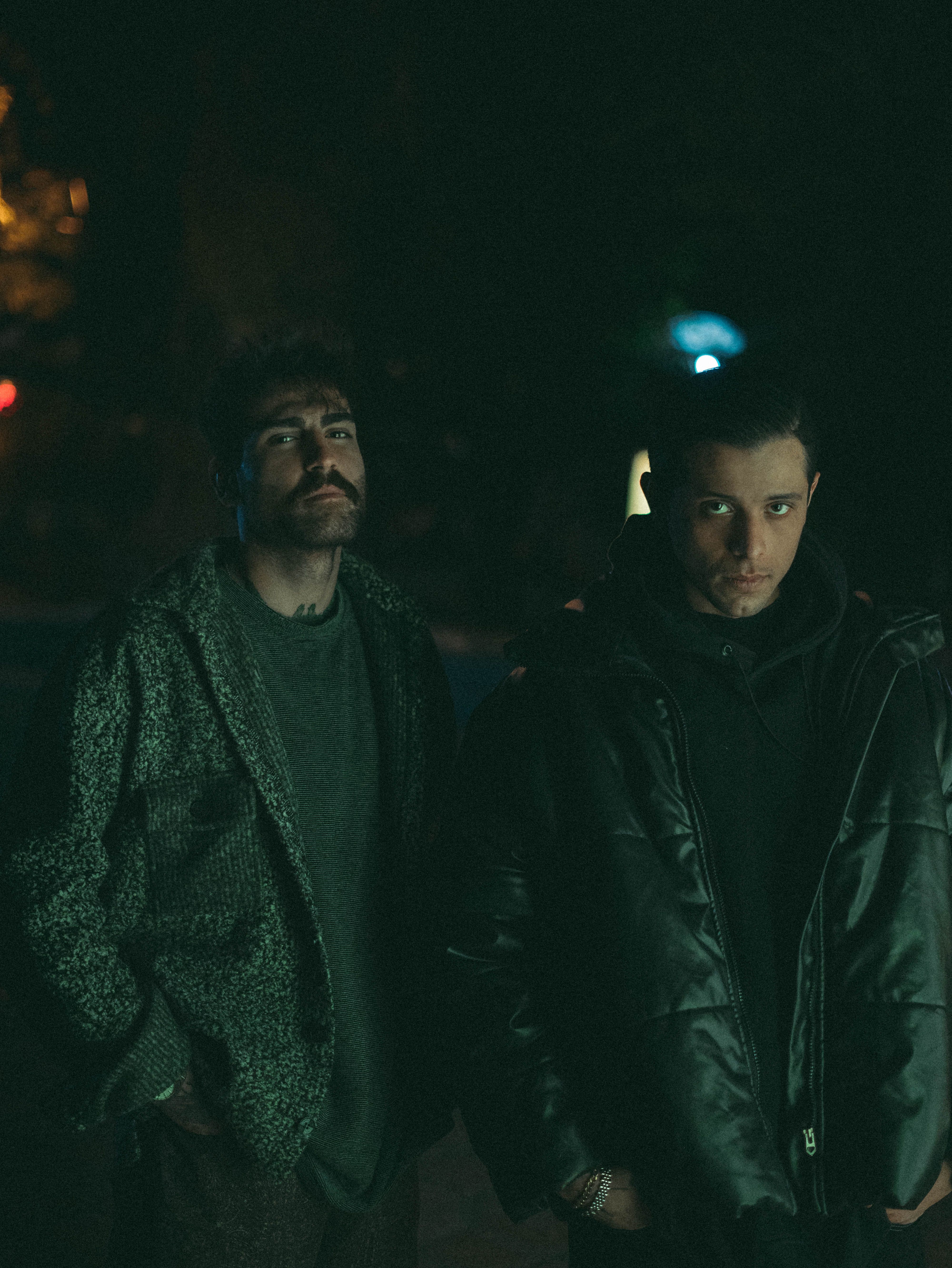 Two men in stylish winter jackets standing outdoors at night, with moody lighting.