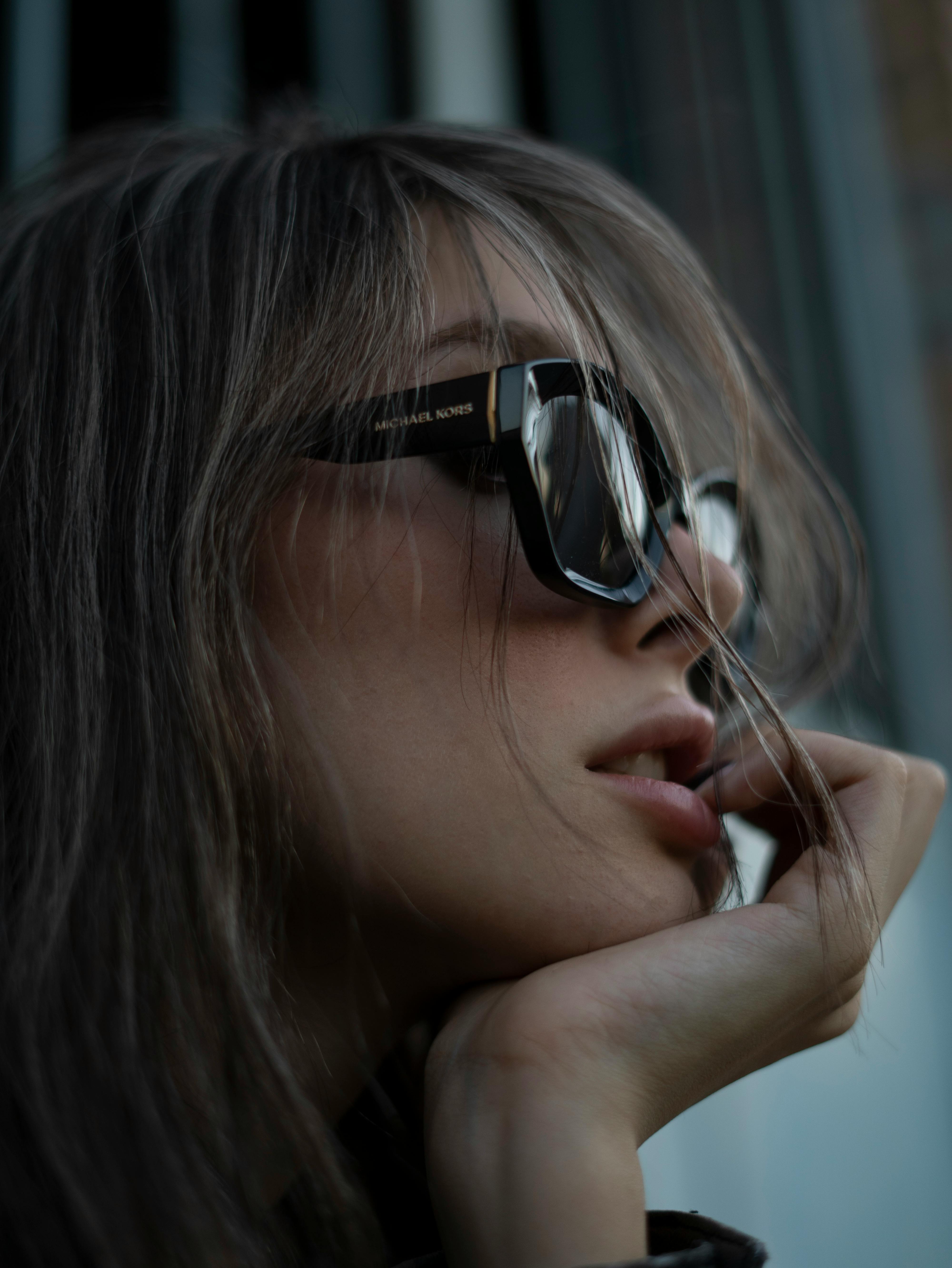 Stylish woman wearing sunglasses, deep in thought, with soft lighting.