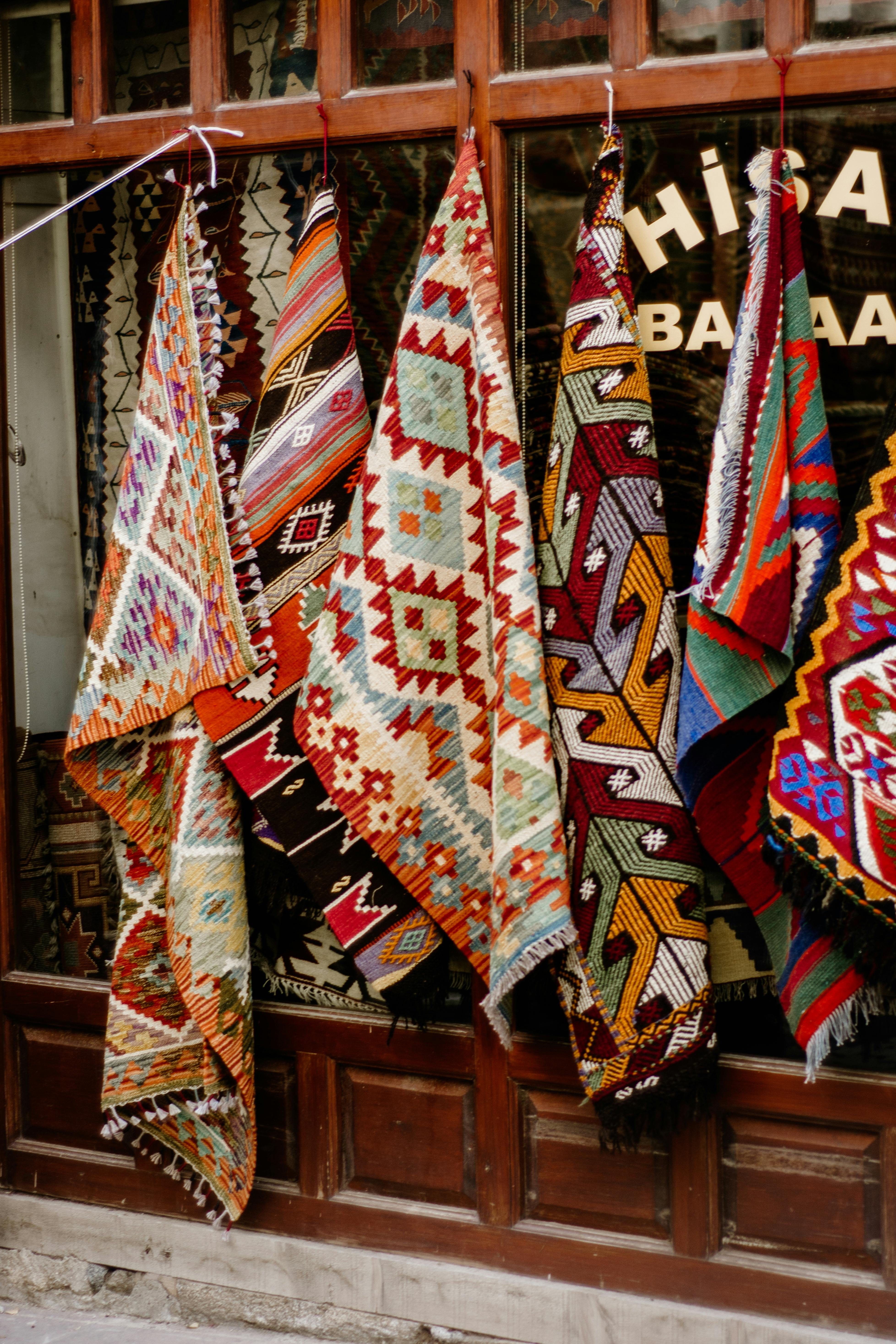 A vibrant collection of traditional patterned rugs hanging at a bazaar shop entrance.