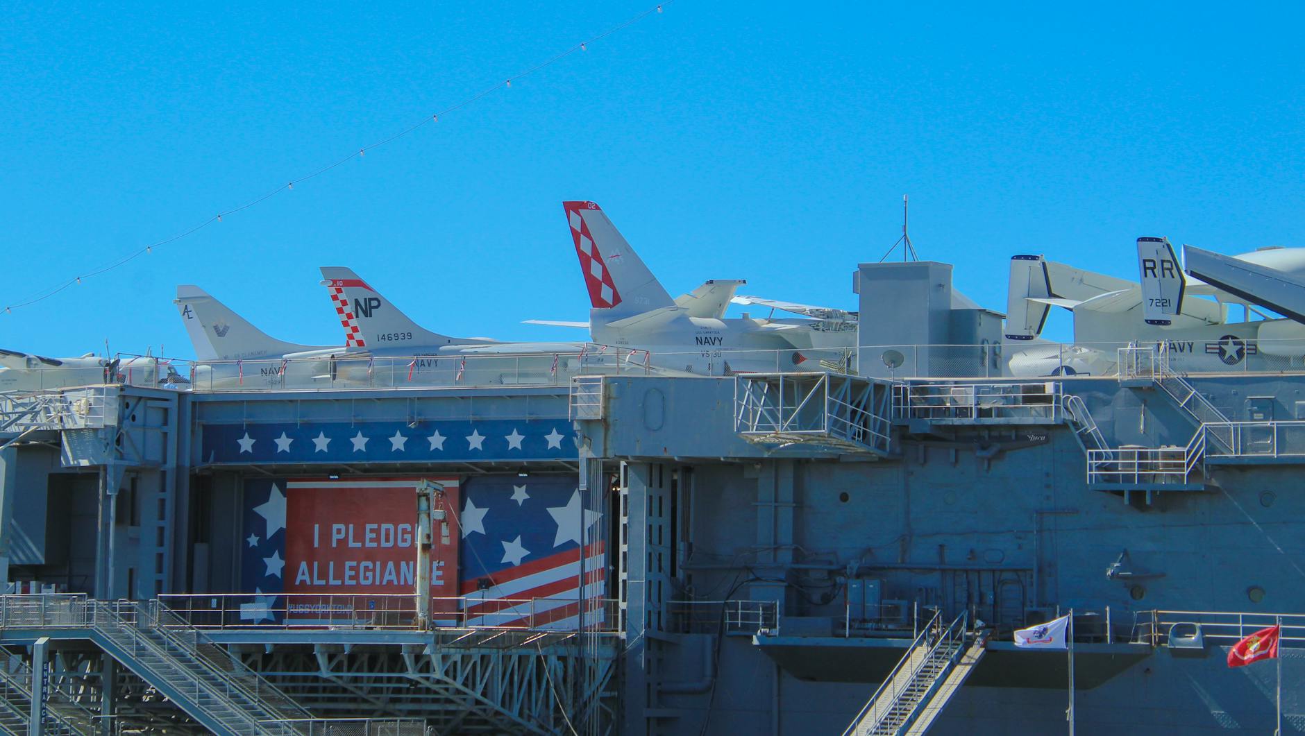 A view of a military aircraft carrier deck with fighter jets and patriotic banner.
