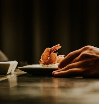 A close-up of a hand placing a plate with shrimp on a table, dimly lit setting.