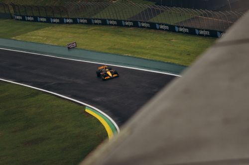 Free An aerial shot of a Formula 1 car racing on a wet track bend, framed by green grass and advertising banners. Stock Photo