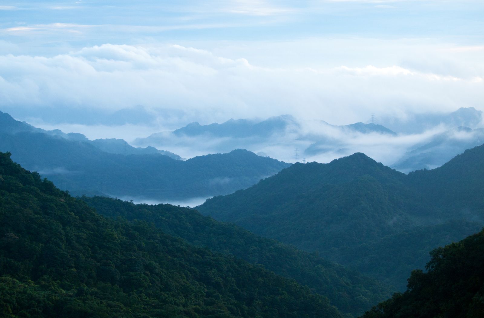 Layered forested ridgelines rising through low cloud at dawn — photo by Alix Lee on Pexels