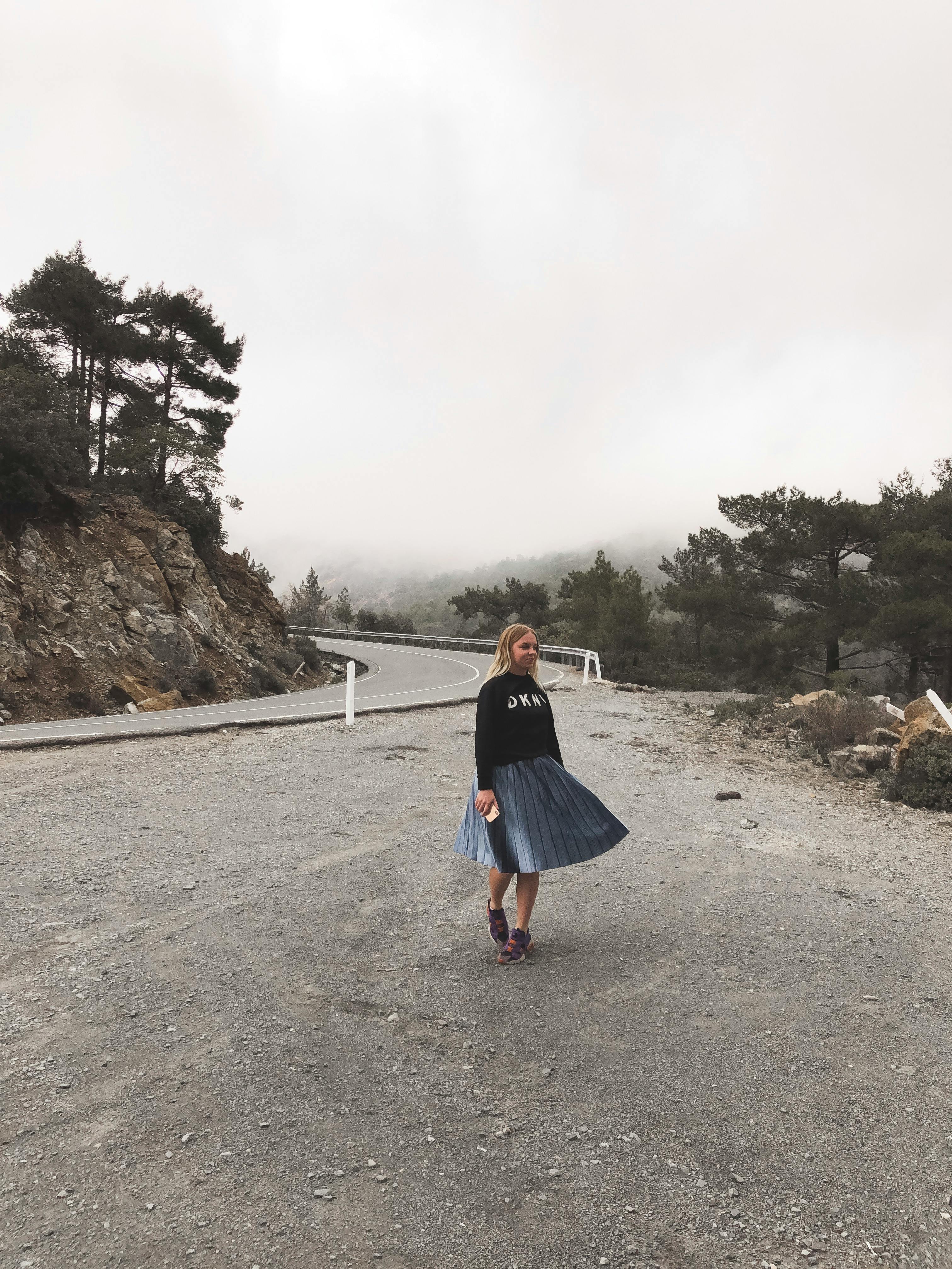 一位年轻女子穿着裙子，站在雾蒙蒙的山路上，捕捉着孤独旅行的心情