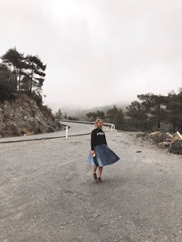 一位年轻女子穿着裙子，站在雾蒙蒙的山路上，捕捉着孤独旅行的心情