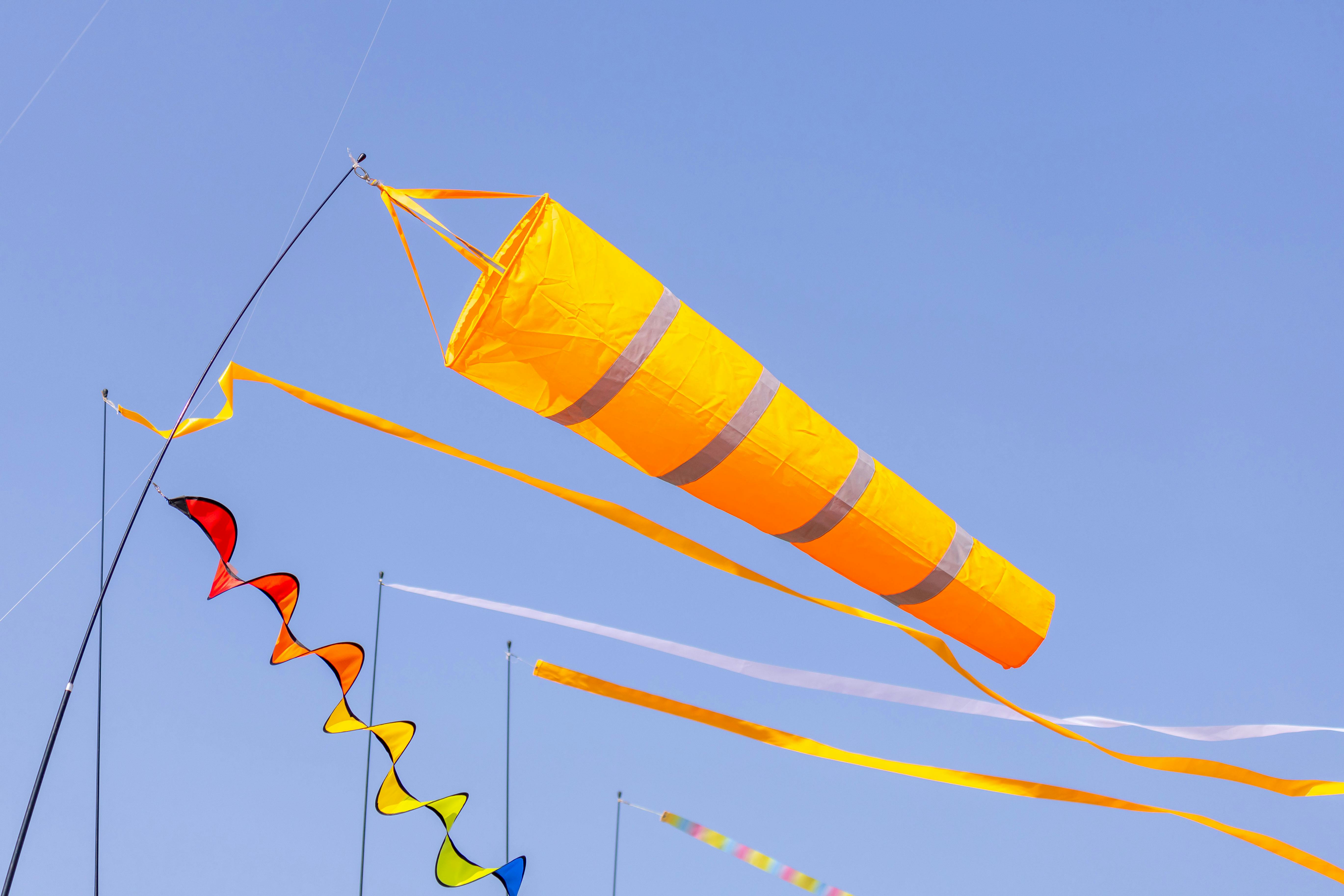 Colorful wind socks and kites fluttering against a clear blue sky, depicting outdoor fun.