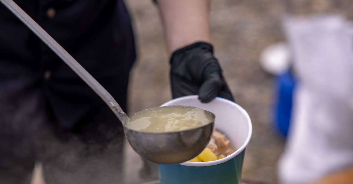 Close-up of a steaming bowl of fufu and palm nut soup being served by a volunteer in a Christ Embassy Loveworld Arena kitchen